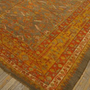 Ornate area rug with olive green field, rust orange and gold borders, lying on weathered wood planks.