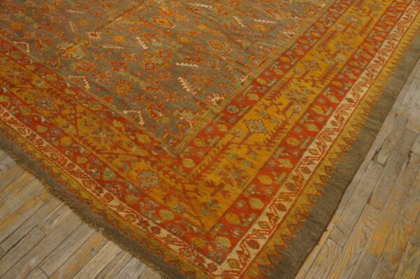 Ornate area rug with olive green field, rust orange and gold borders, lying on weathered wood planks.