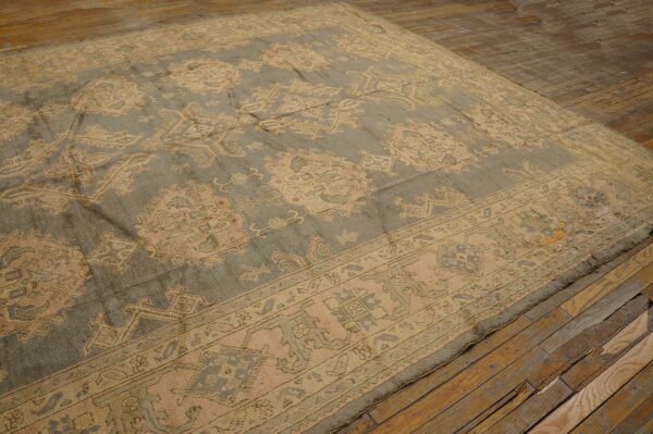 A large traditional rug with dusty sage and peach motifs rests on rustic wood plank flooring.