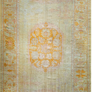 Traditional pale green rug featuring a prominent orange medallion and subtle floral borders on a washed field.