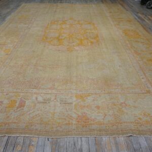 Large beige rug with yellow and orange medallion pattern on distressed wood flooring.