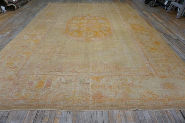 Large beige rug with yellow and orange medallion pattern on distressed wood flooring.