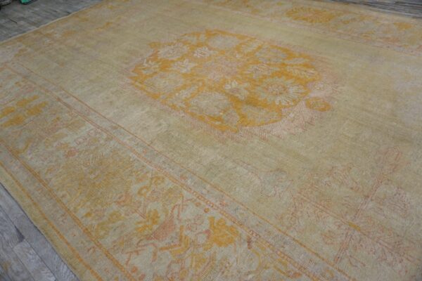 Low-pile rug with a faded beige and yellow floral medallion pattern on gray wood floor.