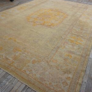 Faded traditional rug featuring a gold medallion and border patterns on distressed wooden flooring.