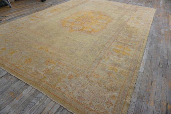 Faded traditional rug featuring a gold medallion and border patterns on distressed wooden flooring.