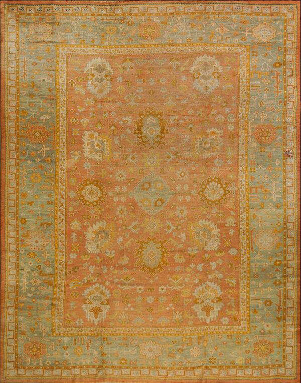 Ornate area rug with a coral field, a wide sage green border, and detailed geometric and floral patterns.