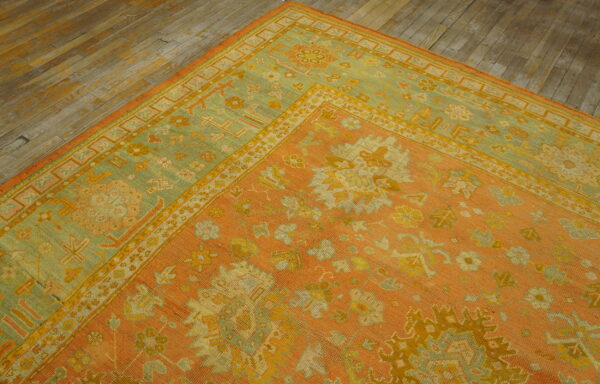 A low-pile rug with apricot, yellow, and faded green ornamental patterns rests on rustic wood flooring.