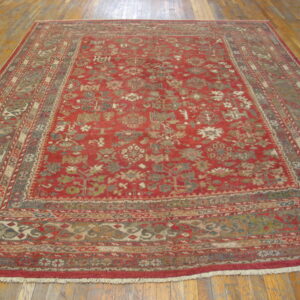 Red traditional rug with intricate motifs and multiple borders, displayed on light brown wood floors.