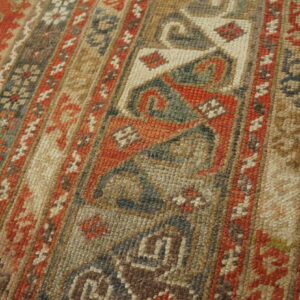 Detailed view of a tightly woven, geometric patterned rug using rust, beige, dark gray, and green tones.