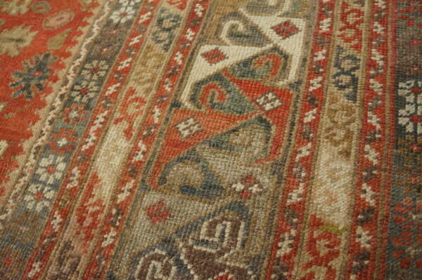Detailed view of a tightly woven, geometric patterned rug using rust, beige, dark gray, and green tones.