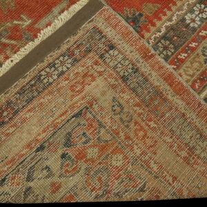 Folded rug corner displays traditional patterns in rust red, beige, and dark earth tones.