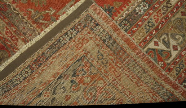 Folded rug corner displays traditional patterns in rust red, beige, and dark earth tones.