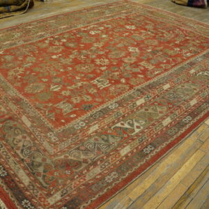 Rusty red rug featuring ornate tan and olive geometric patterns, laid on distressed natural wood planks.