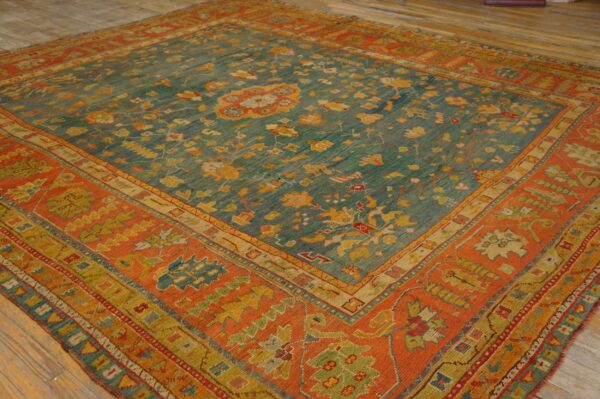 Teal low-pile rug with gold and red motifs, featuring a wide rust-colored patterned border on wood flooring.