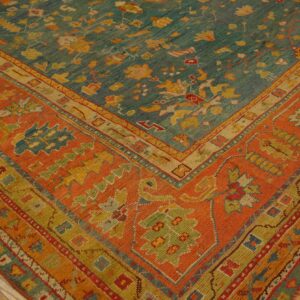 A colorful teal rug with yellow motifs and an orange border rests on worn wood flooring.