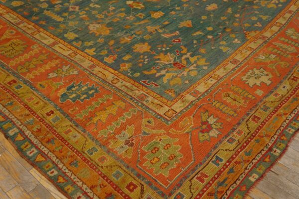 A colorful teal rug with yellow motifs and an orange border rests on worn wood flooring.