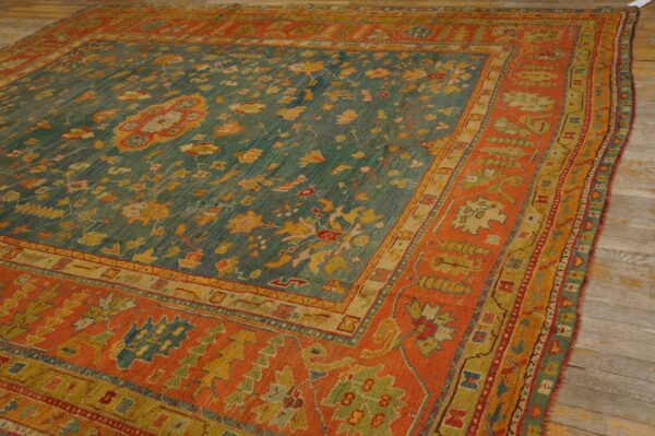 Ornate teal and yellow botanical patterned rug framed by a bold, contrasting orange border on wood planks.