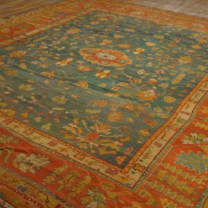 Ornate teal and orange area rug with floral patterns lying on light wood plank flooring.