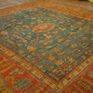 Teal and orange ornamental rug with traditional motifs lying on light wood floors.