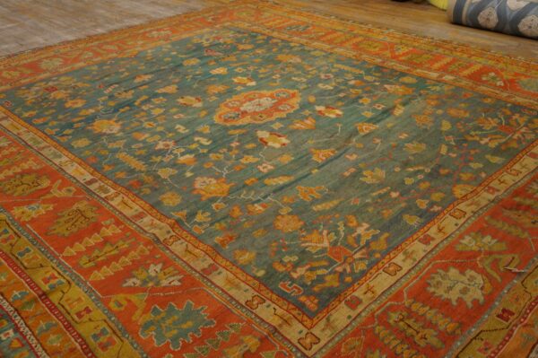Teal and orange ornamental rug with traditional motifs lying on light wood floors.