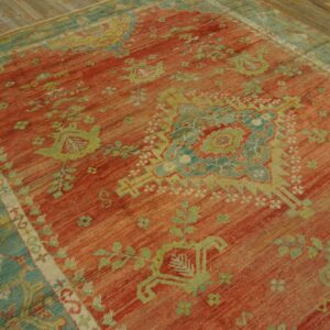 Low-pile rug with a coral red field and light green and blue geometric patterns on distressed wood.
