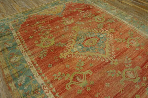 Low-pile rug with a coral red field and light green and blue geometric patterns on distressed wood.