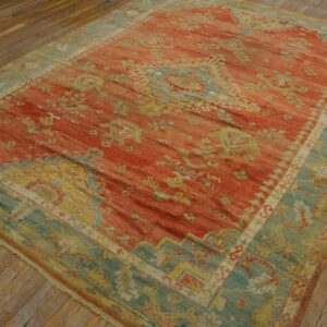 Red and teal traditional patterned rug lying flat on rustic wooden plank floors.