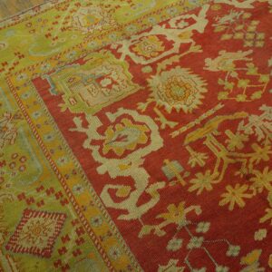 Red field and lime green border rug with detailed patterns rests on distressed wood flooring.