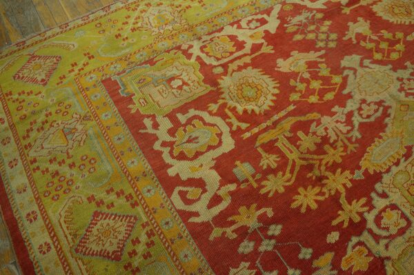 Red field and lime green border rug with detailed patterns rests on distressed wood flooring.
