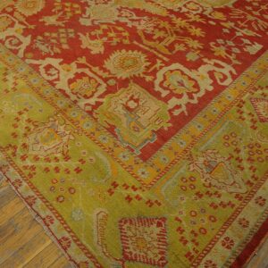 Rust-red and lime-green patterned rug corner featuring detailed geometric designs over distressed wood flooring.