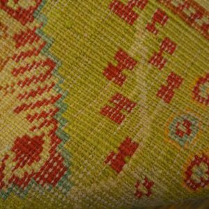Textured flatweave rug detail in chartreuse, yellow, and red with small repeating geometric shapes.