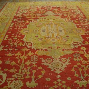 Traditional red and yellow-green rug with central medallion and borders displayed on rustic wood floor.