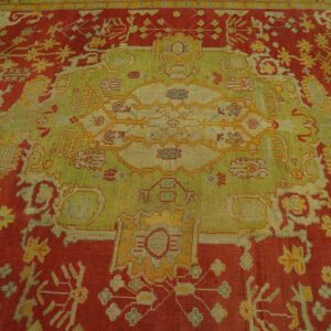 Detailed view of an intricately patterned rug featuring a red field and a large green and gold central design.