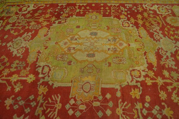 Detailed view of an intricately patterned rug featuring a red field and a large green and gold central design.