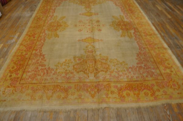 Large traditional rug in pale yellow and orange-pink on rustic plank wood flooring.
