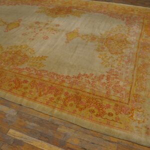 Large pale beige rug with orange and coral floral patterns rests on a distressed plank wood floor.