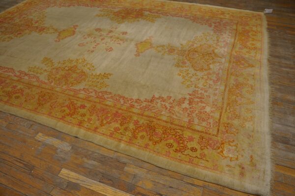 Large pale beige rug with orange and coral floral patterns rests on a distressed plank wood floor.