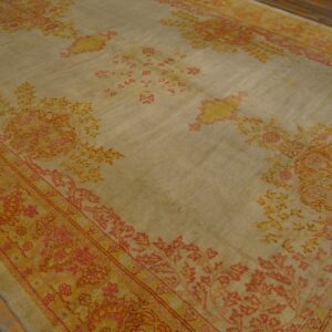 Light taupe rug with faded coral and yellow traditional motifs lying on worn wooden planks.