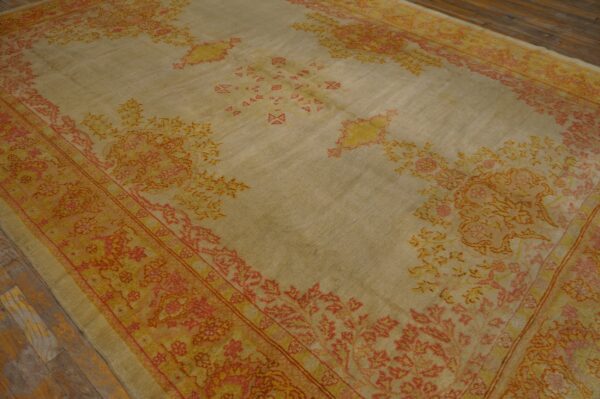 Light taupe rug with faded coral and yellow traditional motifs lying on worn wooden planks.