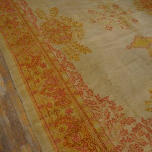 Distressed tan rug with coral and gold traditional border on aged wide plank wood floor.