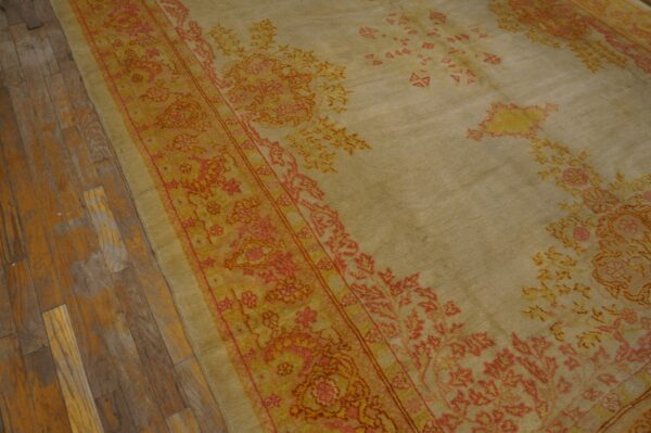 Distressed tan rug with coral and gold traditional border on aged wide plank wood floor.