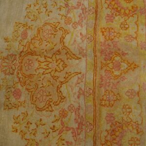 Beige rug with low pile floral patterns in pink, yellow, and orange on visible wooden flooring.