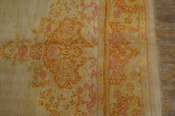 Beige rug with low pile floral patterns in pink, yellow, and orange on visible wooden flooring.