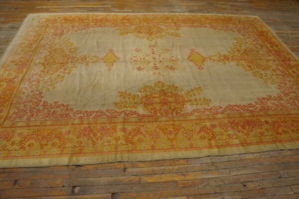 Beige rug with faded gold, orange, and coral traditional patterns on rustic wooden floorboards.