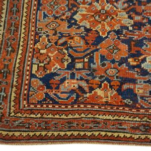 Close-up of a low-pile rug woven with detailed borders in navy, orange, tan, and light blue.
