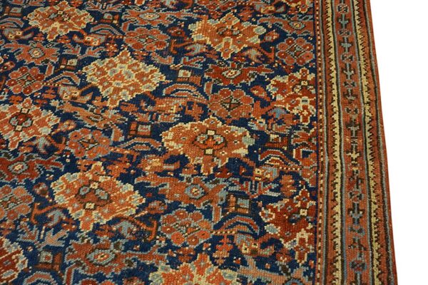 Detailed view of a traditional low-pile rug with a navy blue field and rust orange floral motifs.