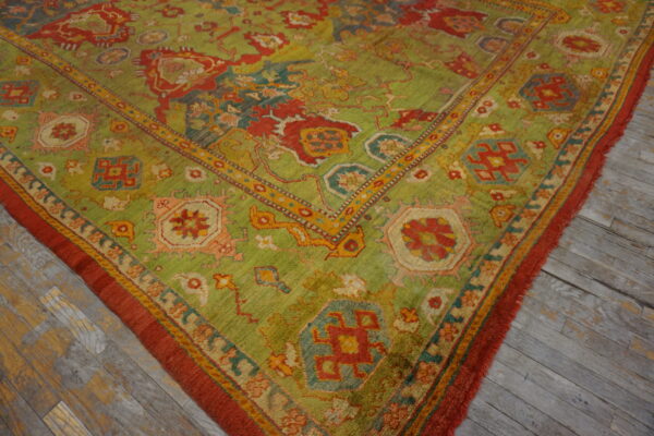 Traditional high-pile rug in green, red, and yellow with complex motifs on gray weathered hardwood flooring.