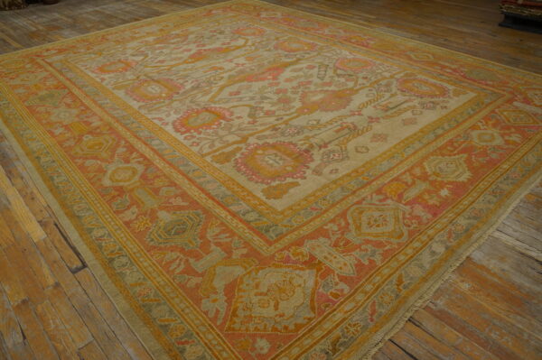 Ornate rug with muted orange, yellow, and beige colors covers rustic wooden floorboards.