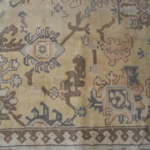 Traditional rug detail showing a tan field with ornate patterns in brown, gray, and dusty rose.