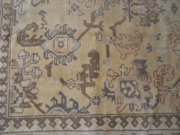 Traditional rug detail showing a tan field with ornate patterns in brown, gray, and dusty rose.
